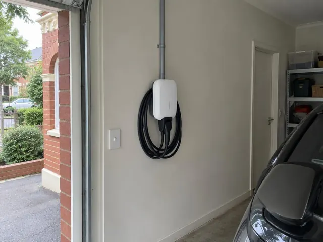 Wall-mounted EV charger with coiled cable in a home garage beside a parked car in Cremorne