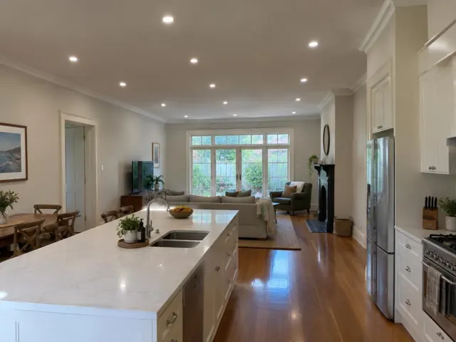 Open-plan living room with recessed ceiling downlights and kitchen island in a modern home in Cammeray