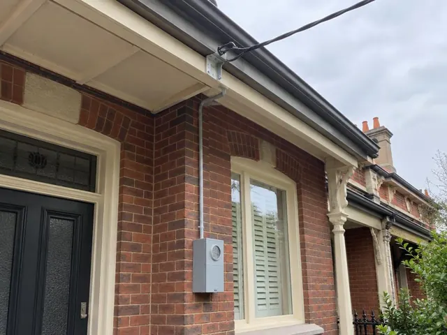 Overhead service cable and point-of-attachment bracket on a brick house facade in North Sydney